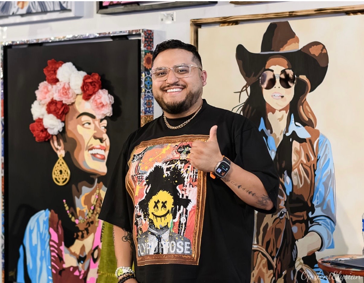 Zeke Martinez smiling and giving a thumbs up between two of his pop art portrait paintings